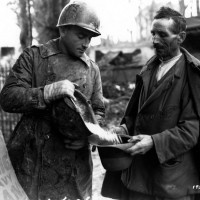 Monghidoro, Appennino bolognese: un ufficiale del Governo militare alleato versa un elmetto pieno di fagioli nel cappello di un civile italiano (2 novembre 1944),  foto in archivio dell'Istituto per la storia e le memorie del '900 Parri Emilia-Romagna.
